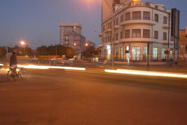Street corner with a curved modernist building and light trails from passing traffic at dusk in central Asmara, Eritrea