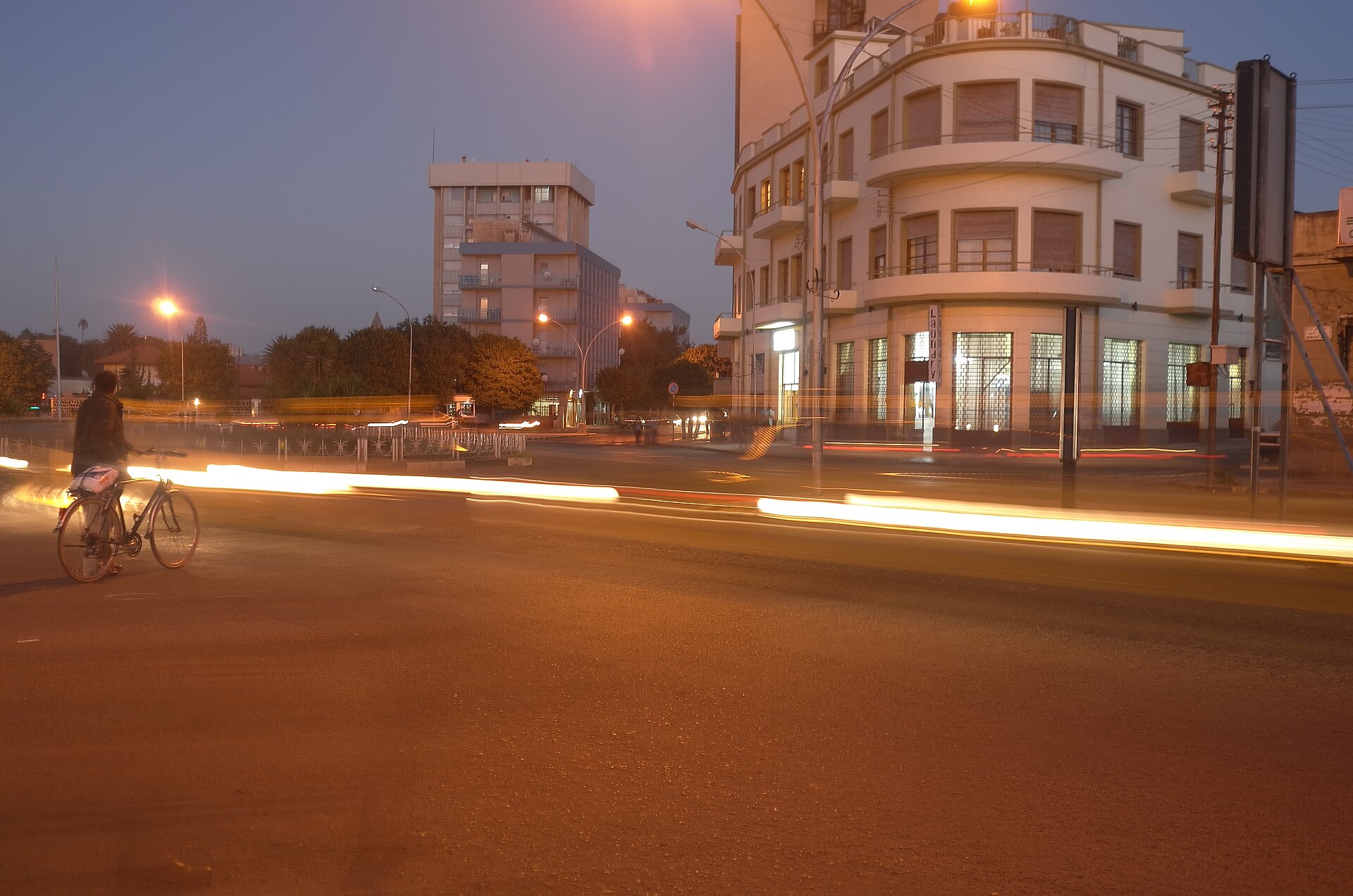 Street corner with a curved modernist building and light trails from passing traffic at dusk in central Asmara, Eritrea