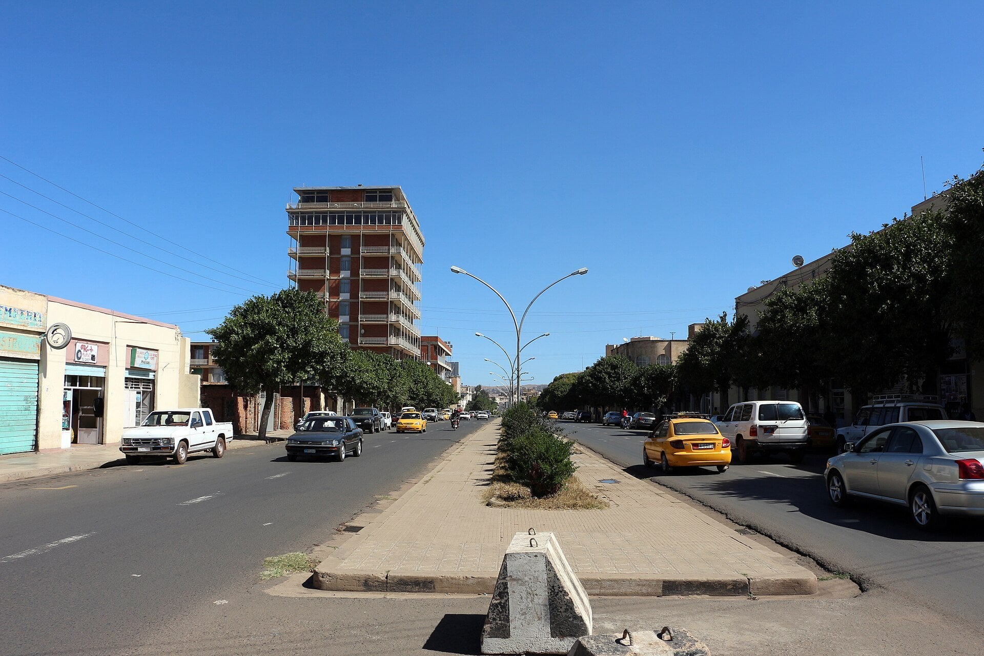 Taxis and cars on a tree-lined avenue with a central median and a high-rise in Asmara, Eritrea