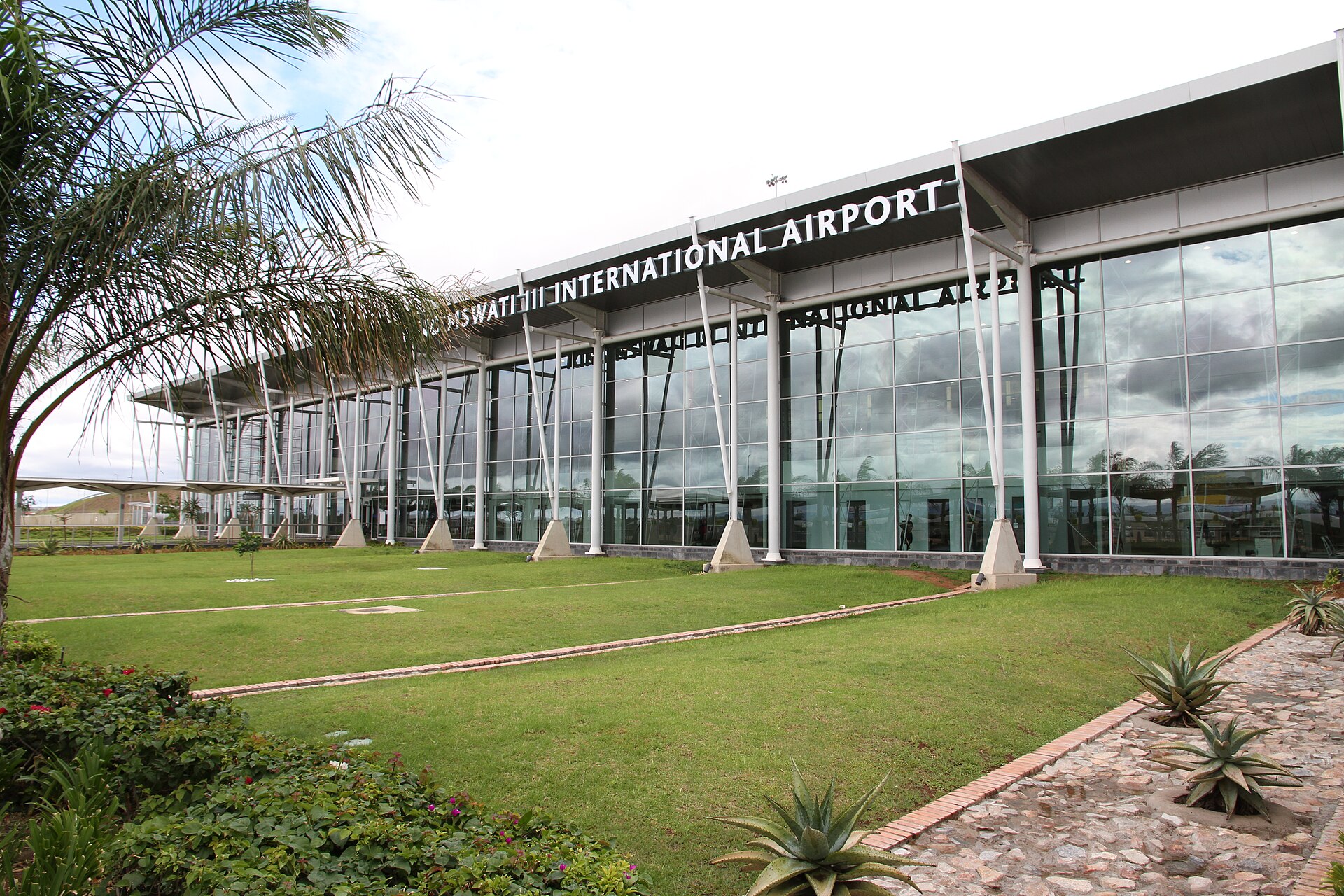 Glass-fronted terminal building of King Mswati III International Airport in Eswatini, with lawns and palm trees in front