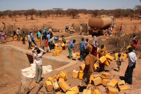 Villagers with yellow jerrycans gather at a water point beside a water tanker truck on dry, red ground in Ethiopia