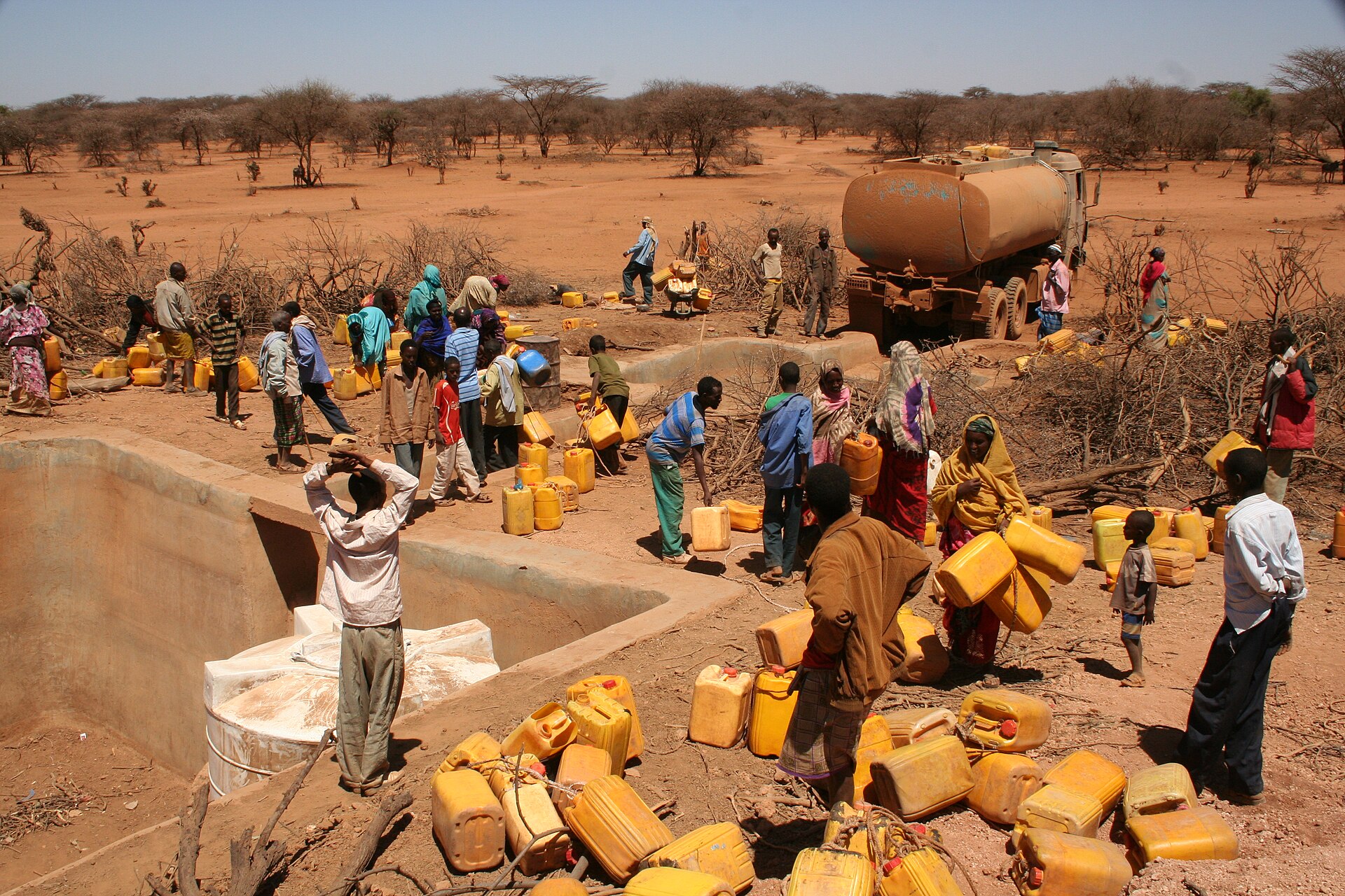 Villagers with yellow jerrycans gather at a water point beside a water tanker truck on dry, red ground in Ethiopia