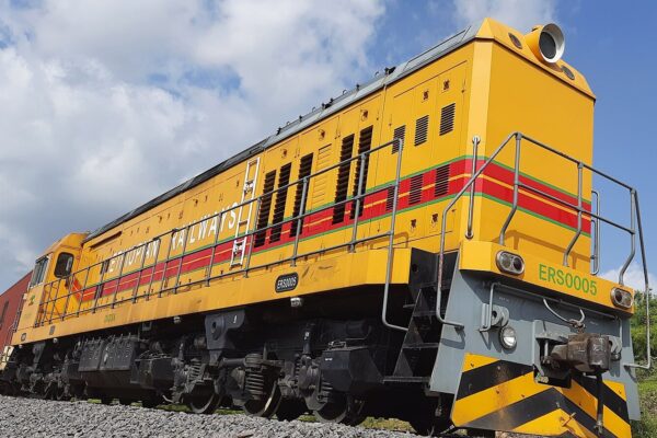 An Ethiopian Railways locomotive in yellow, red and green livery pulling container wagons at Mojo station under a blue sky