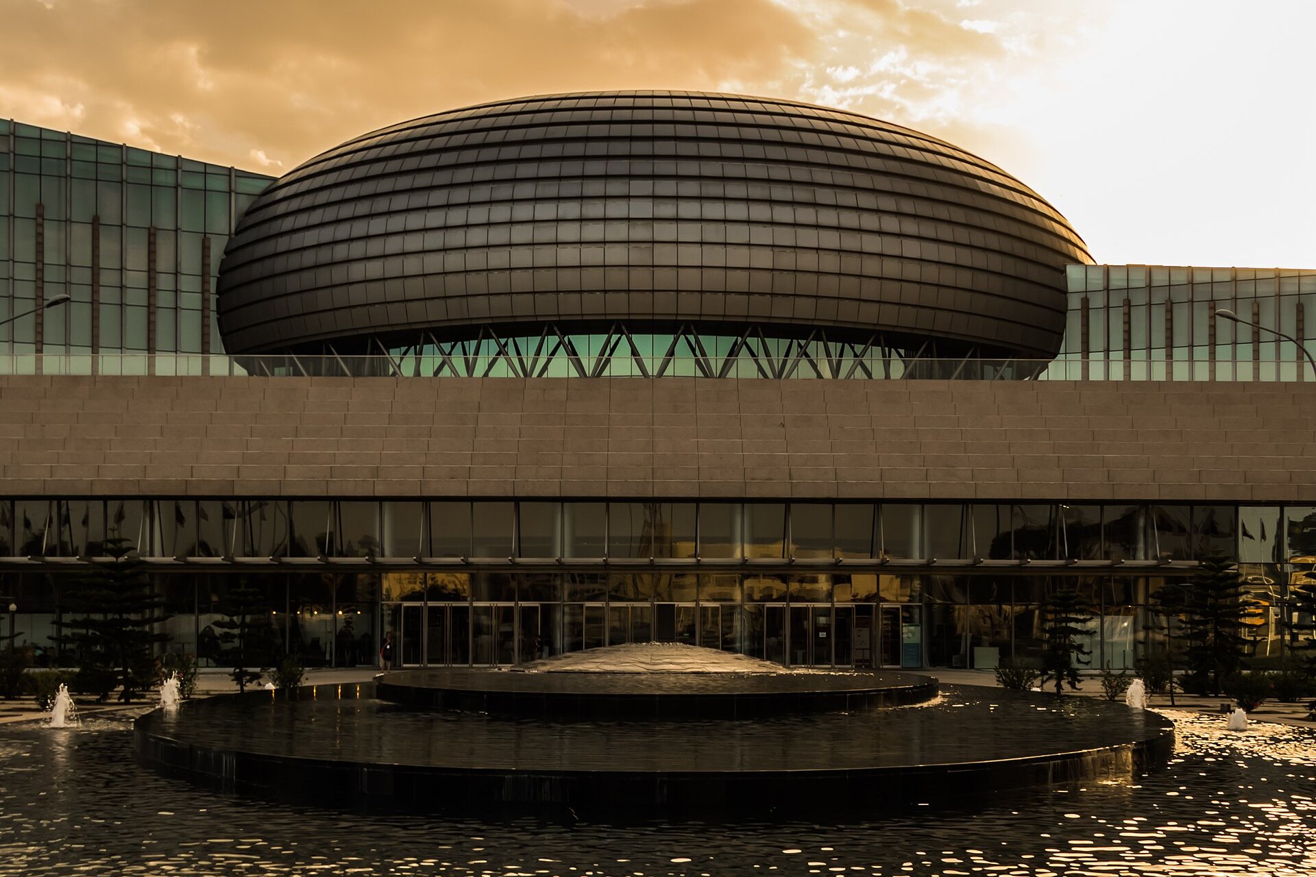 The domed African Union Conference Centre in Addis Ababa at sunset with a fountain pond in front of its glass facade