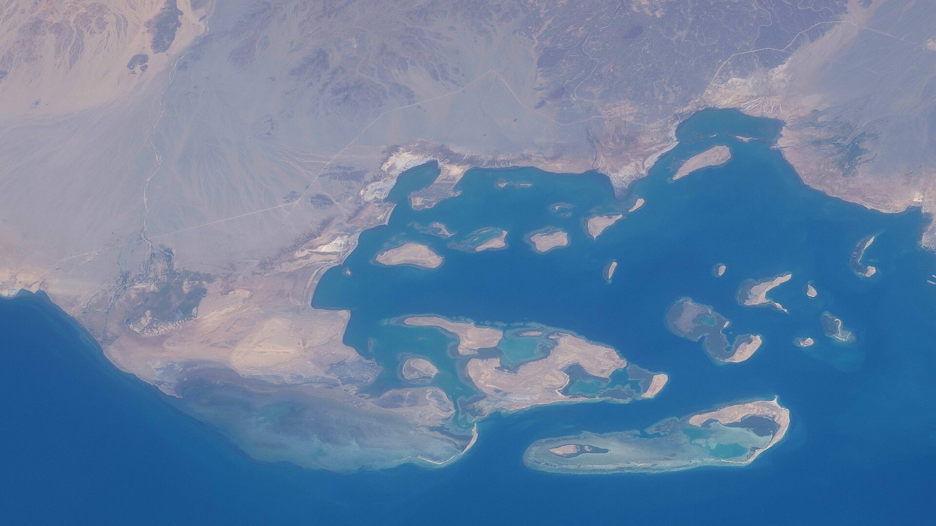 Satellite-style view of Assab Bay on Eritrea's Red Sea coast with islands and reefs in deep blue water beside a desert shoreline