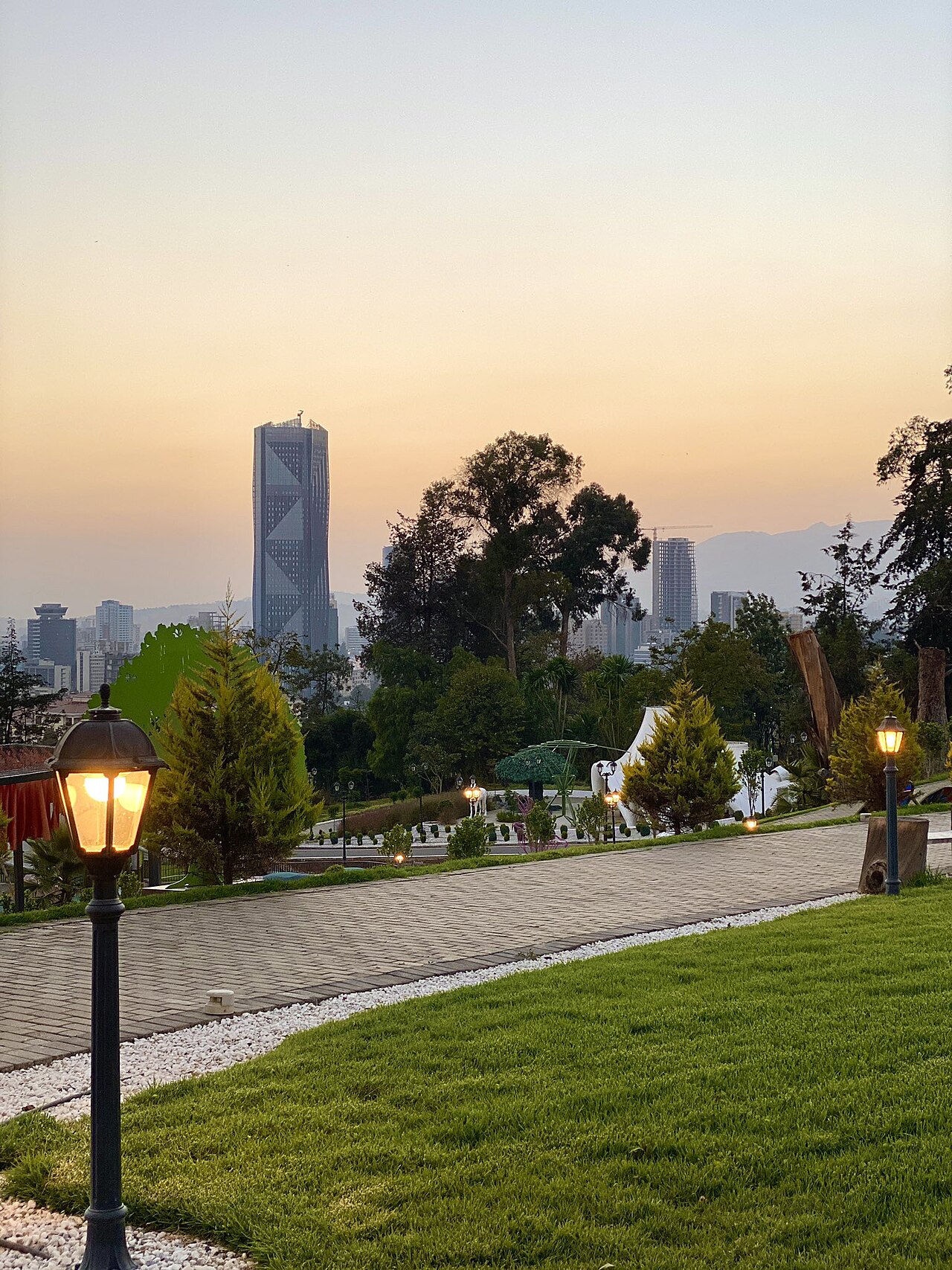 Lamp-lit garden path in Unity Park with Addis Ababa high-rise towers behind at dusk