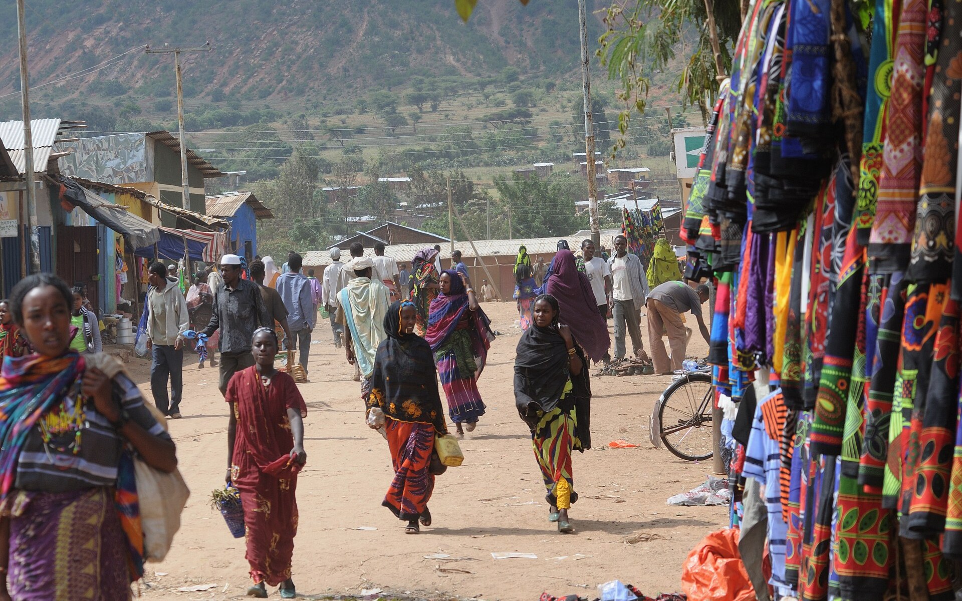 Women and men walk along the market street in Yabelo, southern Ethiopia, past stalls hung with colourful cloth