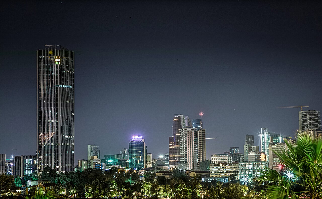 Addis Ababa skyline at night with a tall glass tower on the left and lit office buildings below a dark sky