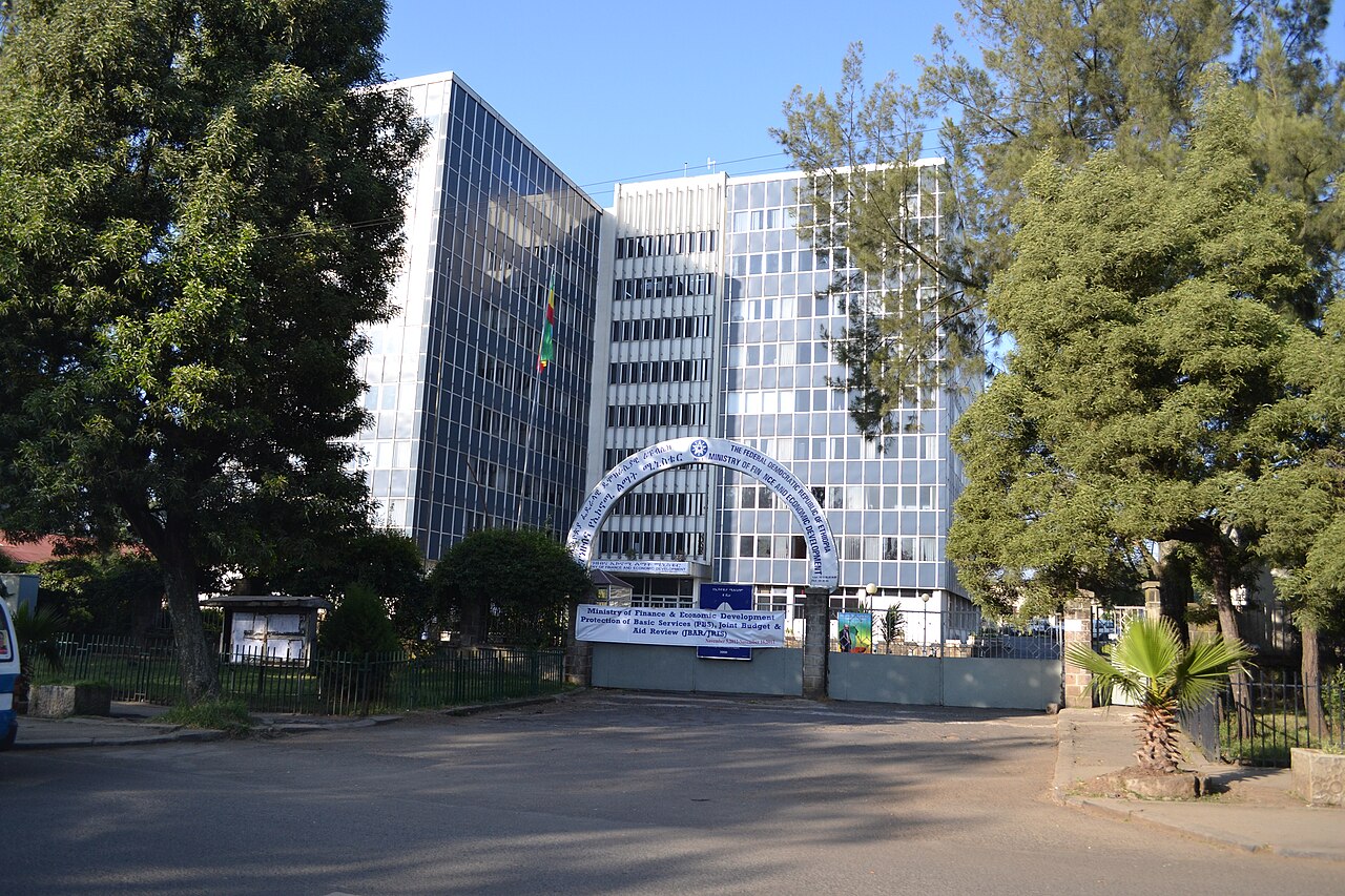 Glass-fronted Ministry of Finance offices in Addis Ababa seen from the street, with trees and an entrance arch
