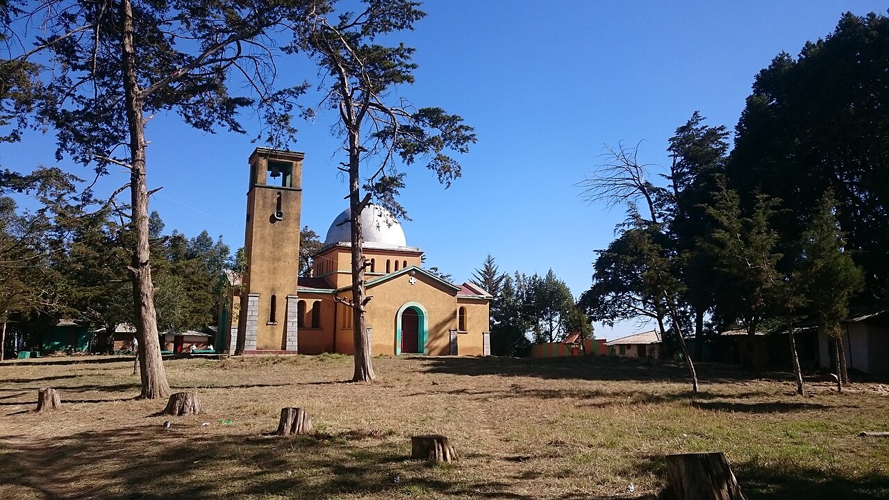 An Ethiopian Orthodox church with a bell tower and white dome among cypress trees, in Ejersa Goro, Ethiopia