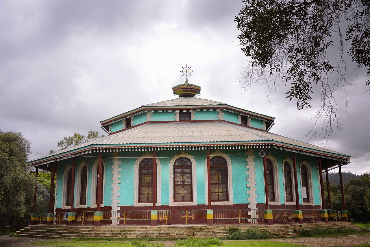 An eight-sided Ethiopian Orthodox church with turquoise walls and a metal roof under a cloudy sky in Adigrat, Ethiopia