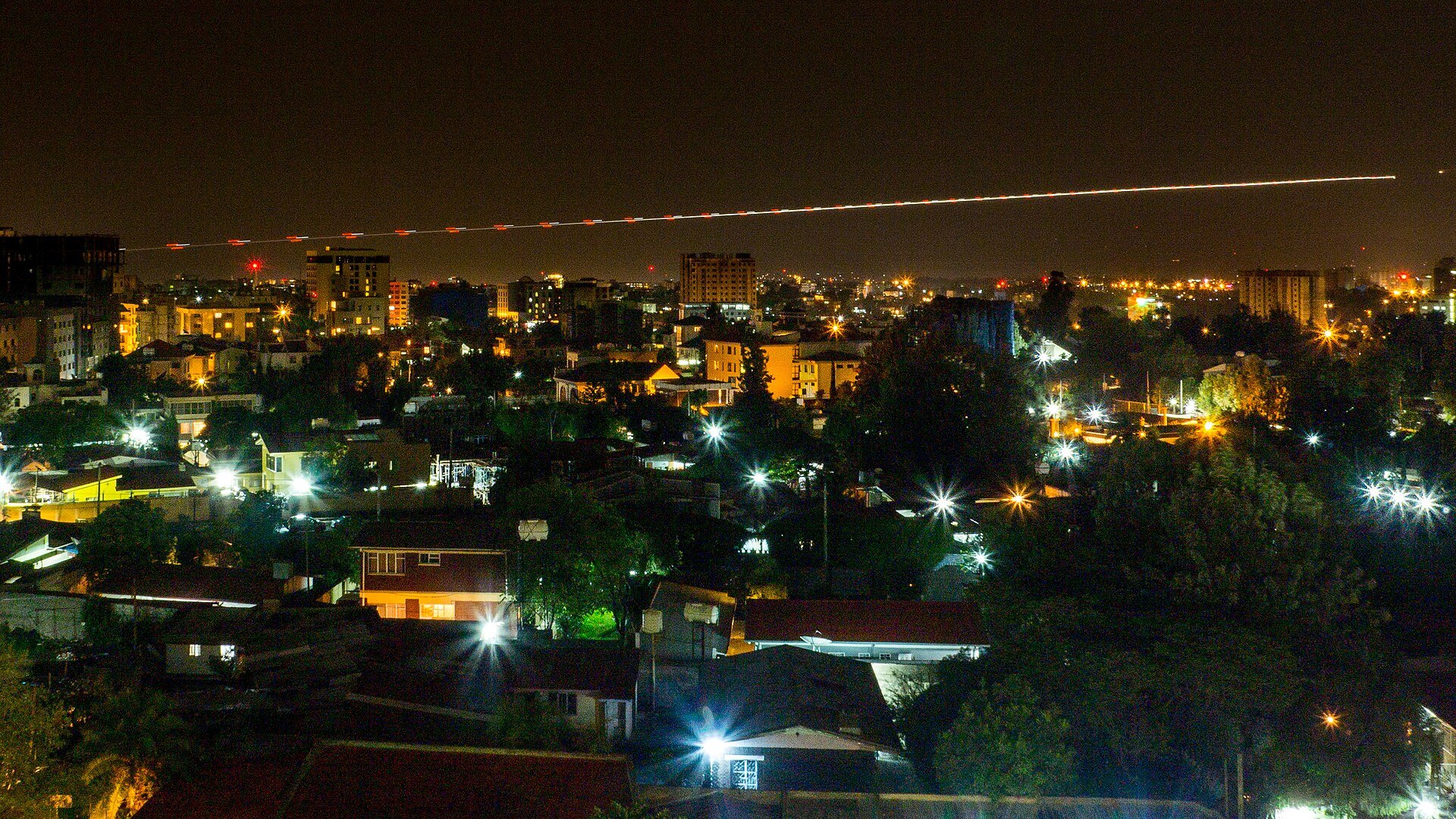 Night view over the lit rooftops of Addis Ababa with the long light trail of an aircraft landing at Bole airport