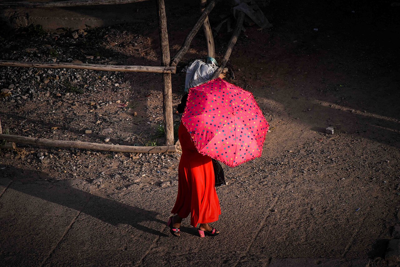 A woman with a red umbrella walks along a street in Adigrat, Tigray