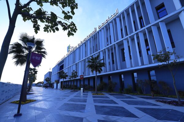 Palm-lined promenade and a white-louvred building with Arabic signage at Euromed University of Fès at dusk