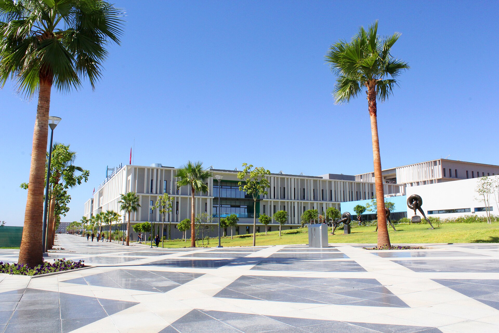 Palm-lined paved promenade and low white buildings on the Euromed University of Fès campus in sunshine