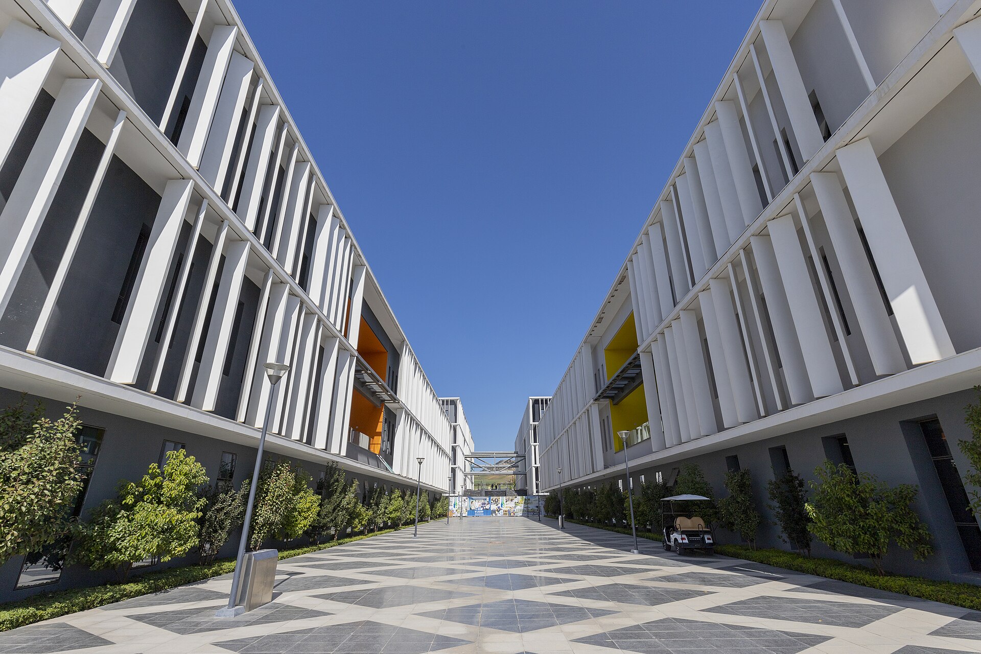 Paved avenue between two white-louvred teaching buildings with orange and yellow accents at Euromed University of Fès