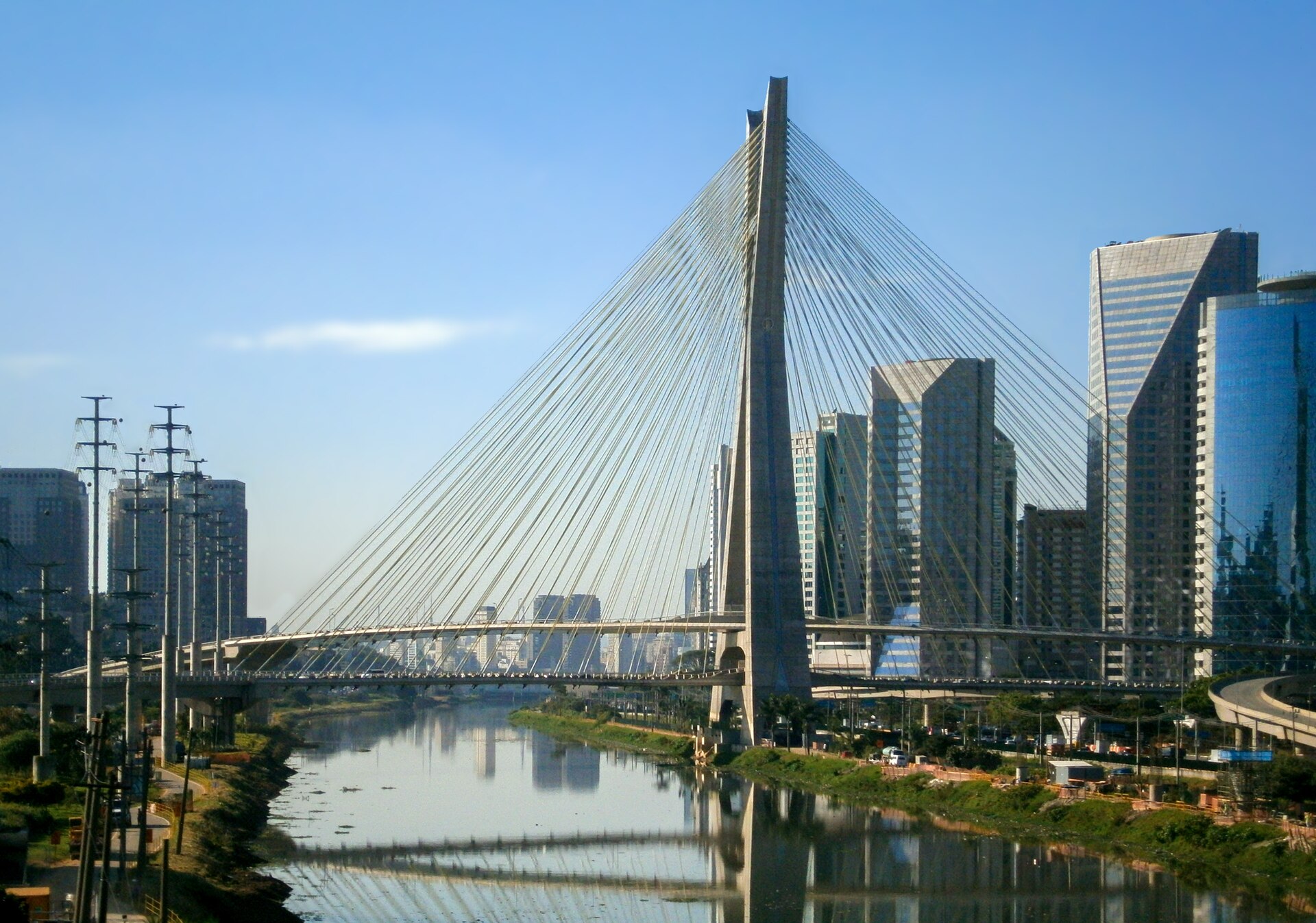 The cable-stayed Octávio Frias de Oliveira bridge over the Pinheiros River with office towers on the right bank under a clear sky