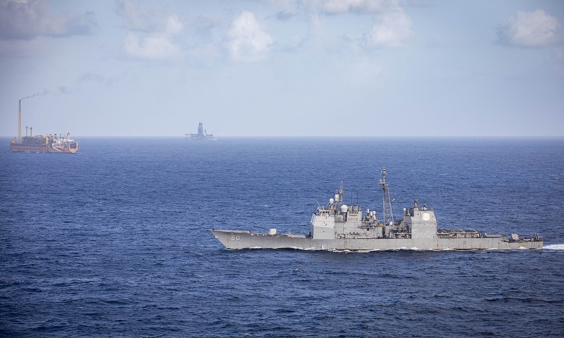 A US Navy cruiser passes floating oil production vessels in the Stabroek Block off Guyana
