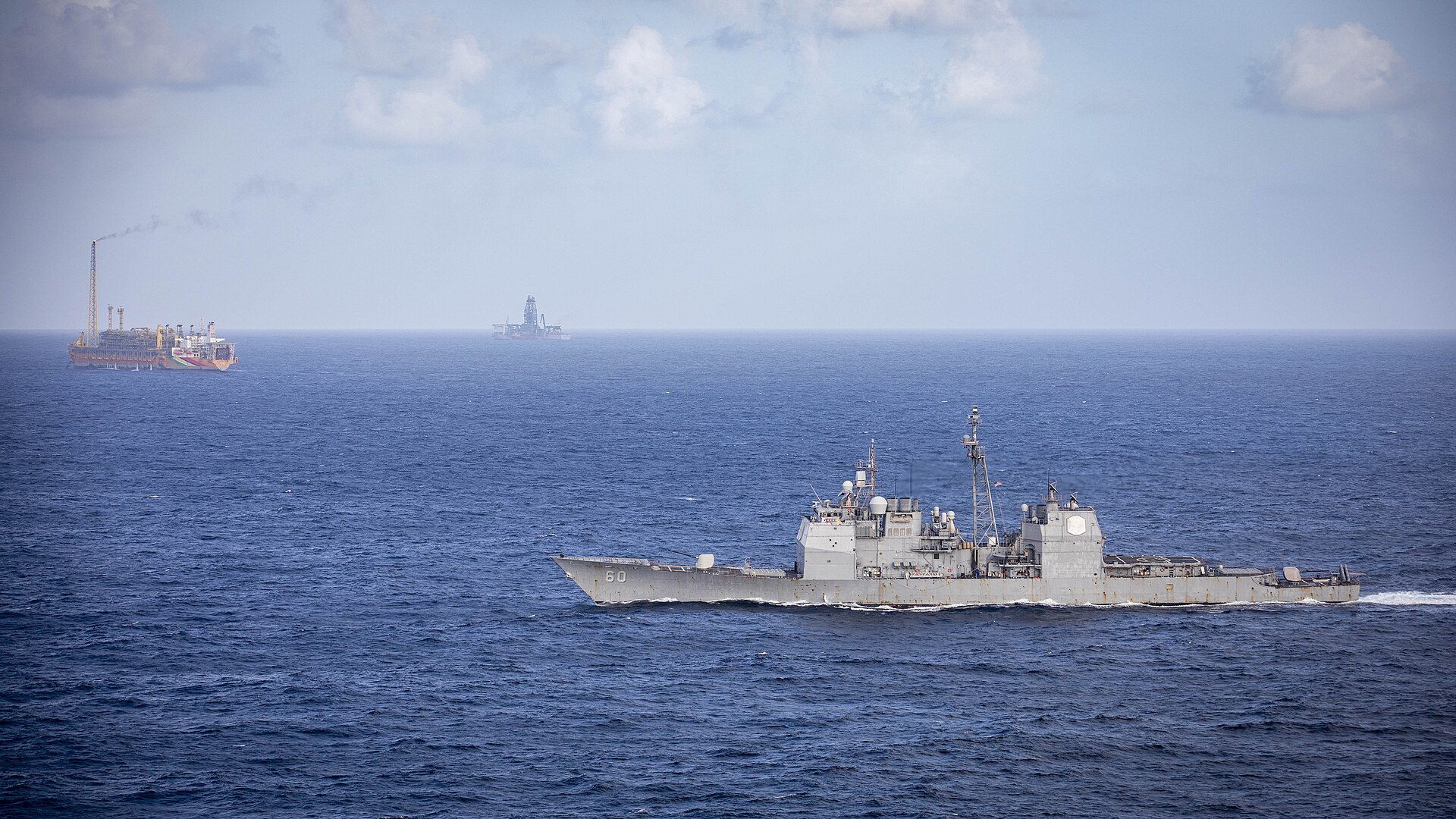 A US Navy cruiser passes floating oil production vessels in the Stabroek Block off Guyana