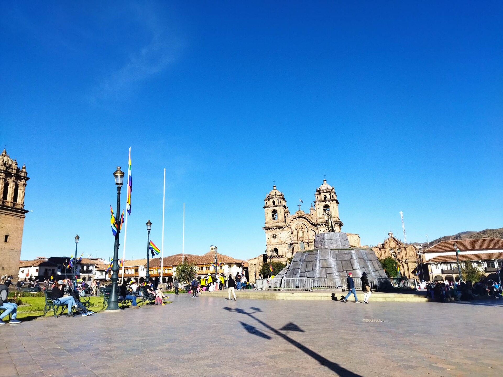 The Plaza de Armas in Cusco under a blue sky, with the Church of the Company of Jesus in the centre and the edge of Cusco Cathedral at left
