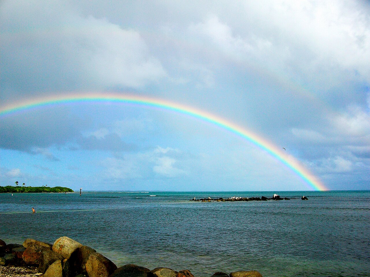 The coast at Las Croabas in Fajardo, Puerto Rico, with a rainbow over the sea and a small island on the horizon