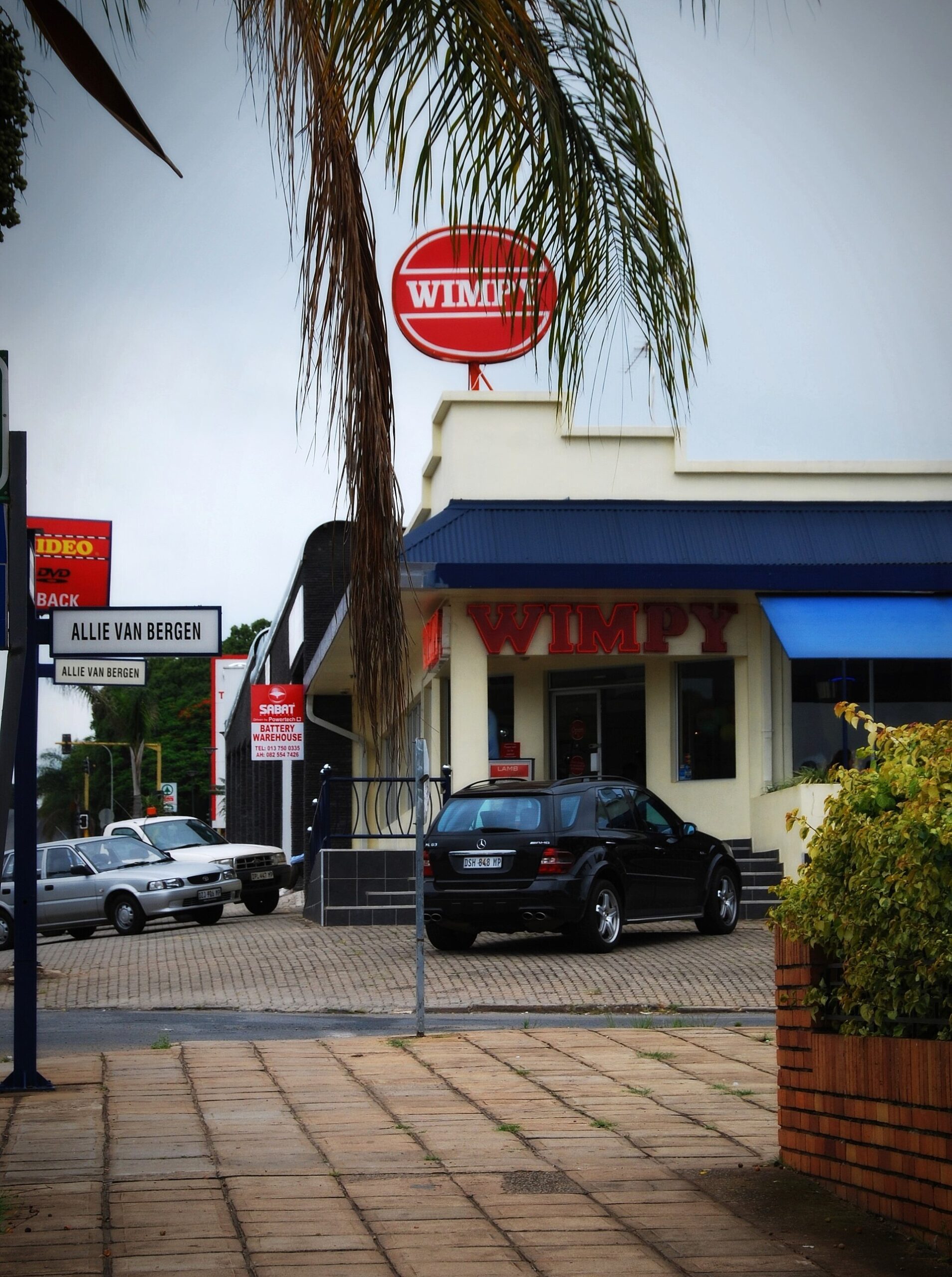 A Wimpy restaurant with a red oval sign above a cream building on a street corner in White River, South Africa