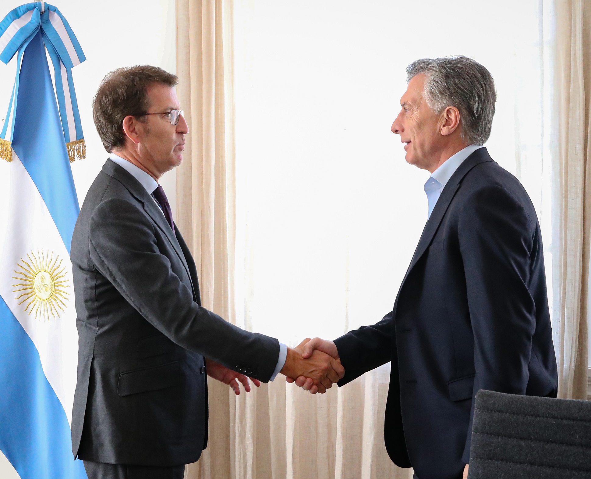 Alberto Núñez Feijóo shakes hands with Argentine President Mauricio Macri next to an Argentine flag