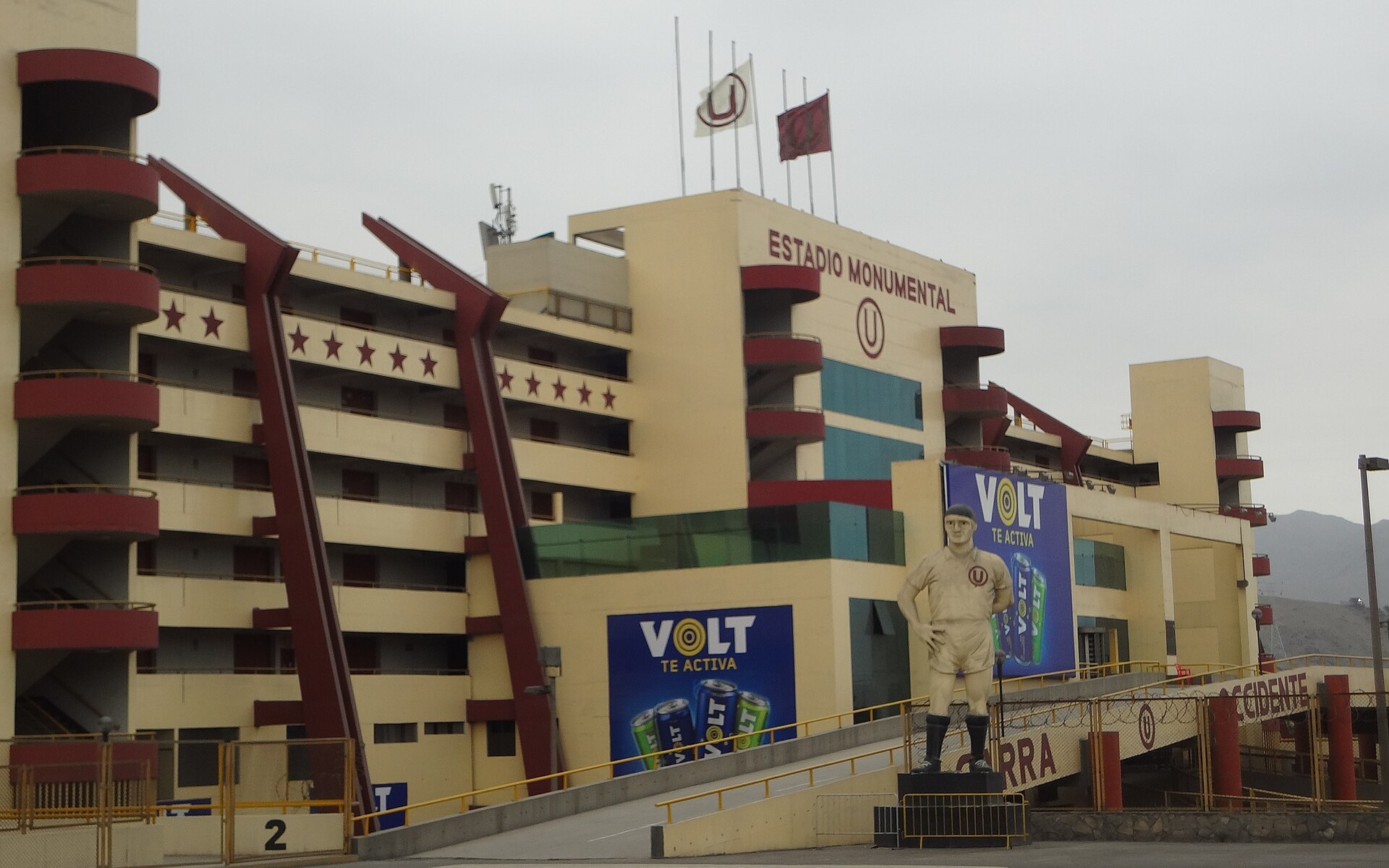 The main facade of the Estadio Monumental in Ate, Lima, Peru, with red stairwells, a player statue and club flags