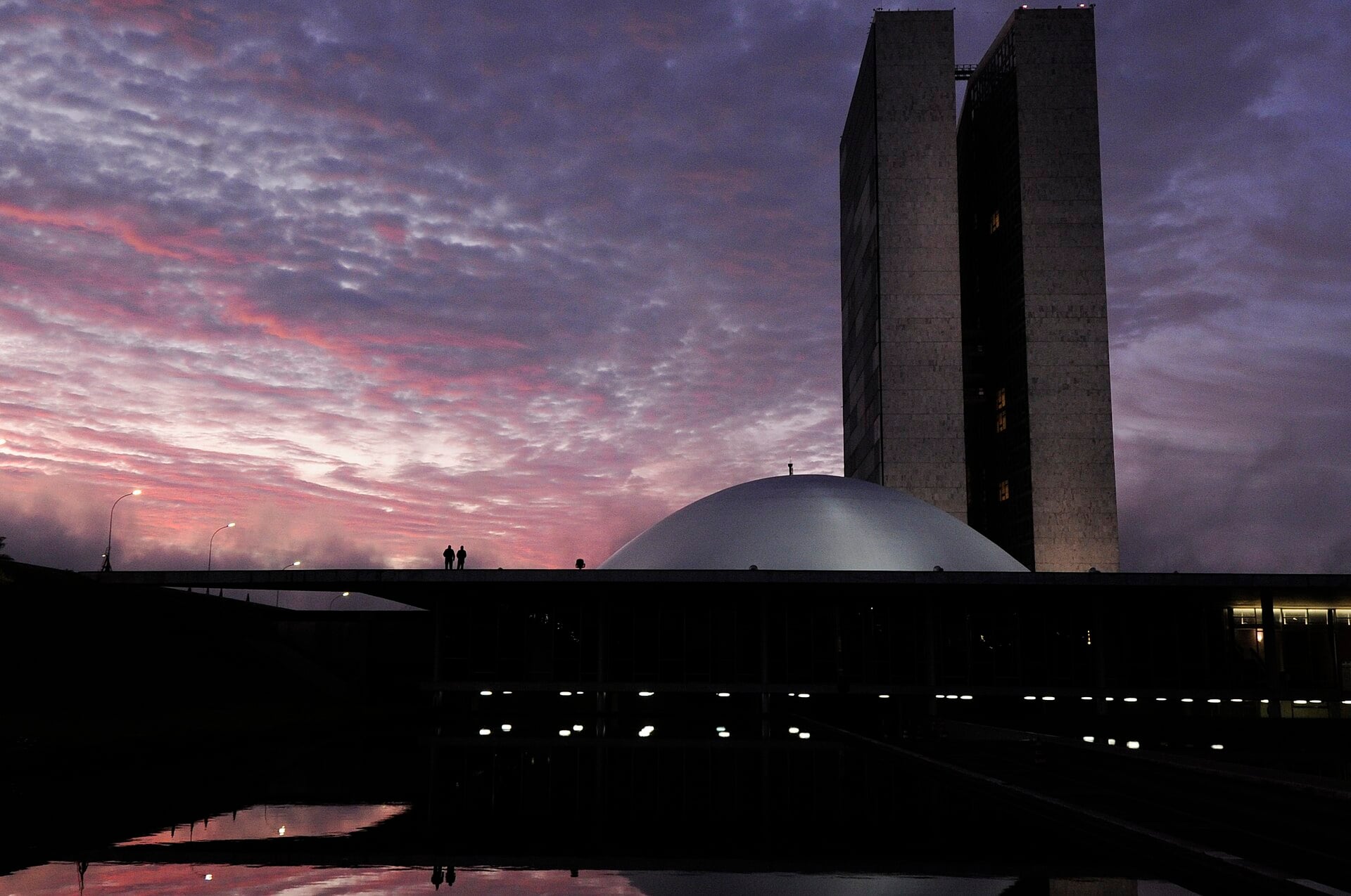 The National Congress in Brasília at dawn, with the twin office towers and the Senate dome silhouetted against a pink and purple sky