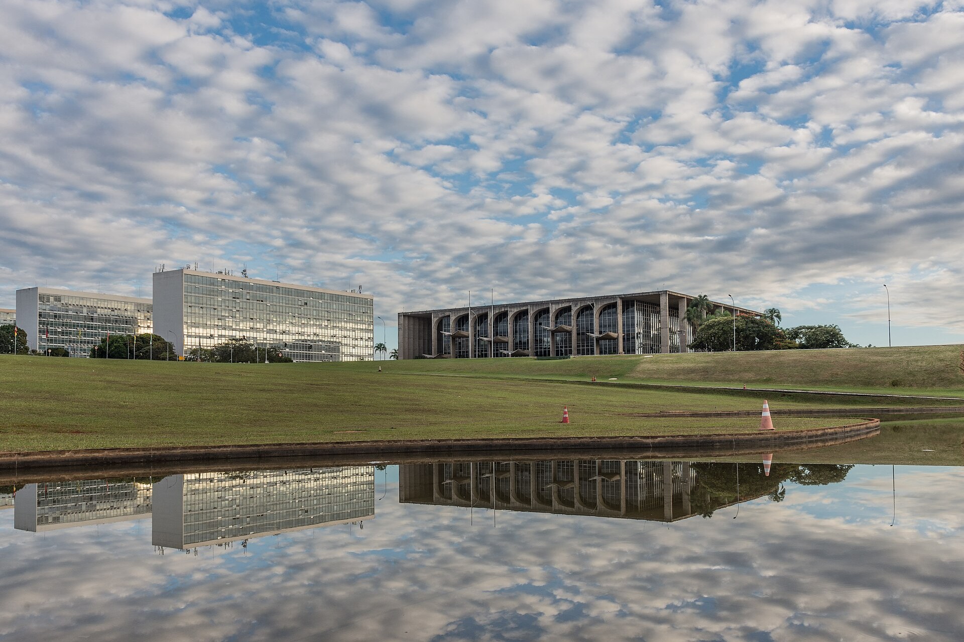 The Palácio da Justiça, a low Niemeyer building with arched glass bays, and two ministry office blocks in Brasília, reflected with a cloudy sky in a pool