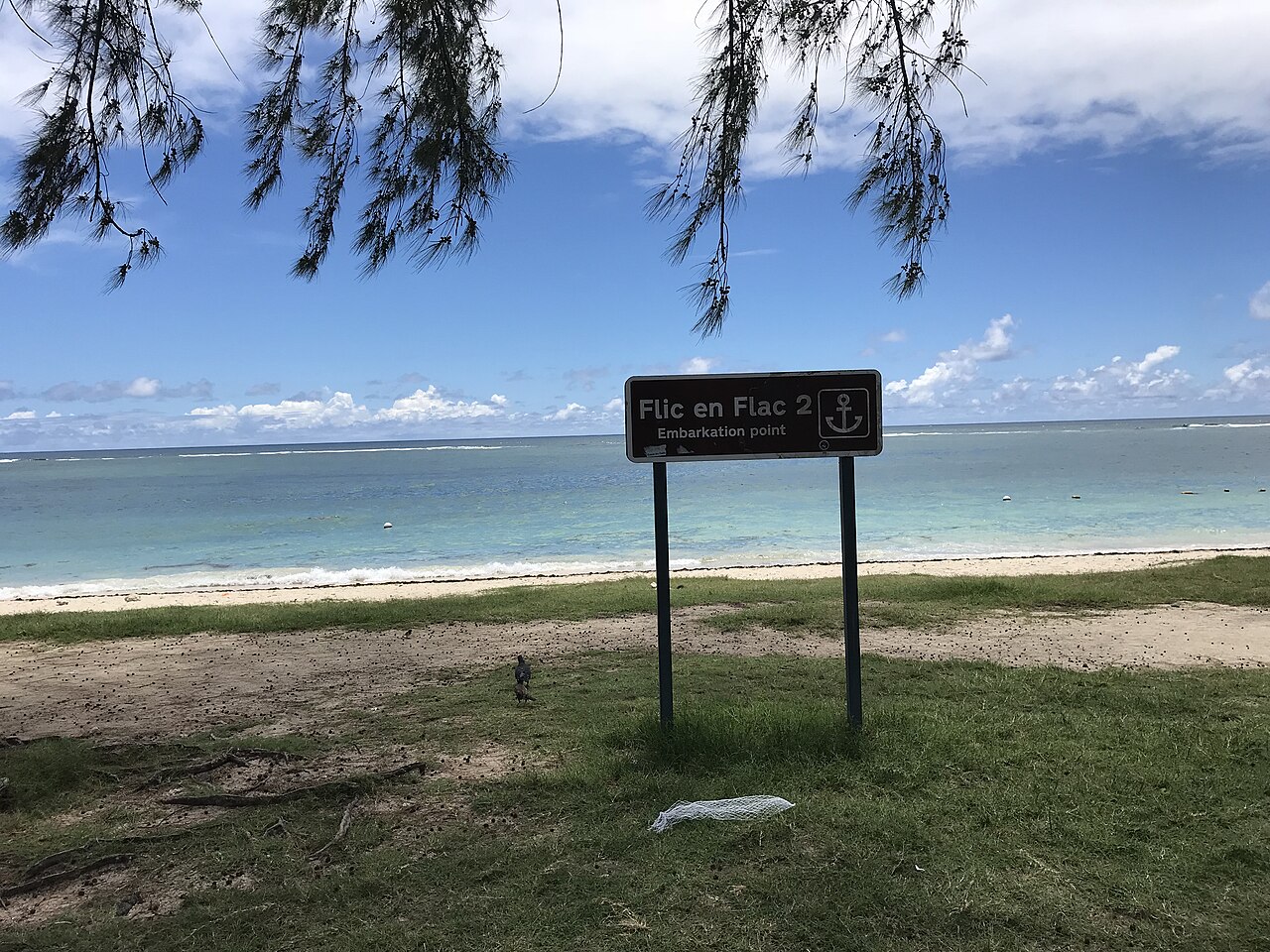 A beach sign reading Flic en Flac 2 above a turquoise lagoon on the west coast of Mauritius.