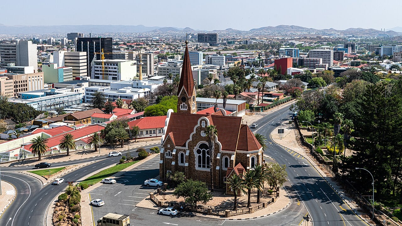 Christ Church, a red-roofed stone church with a tall spire, stands among office buildings in central Windhoek, Namibia