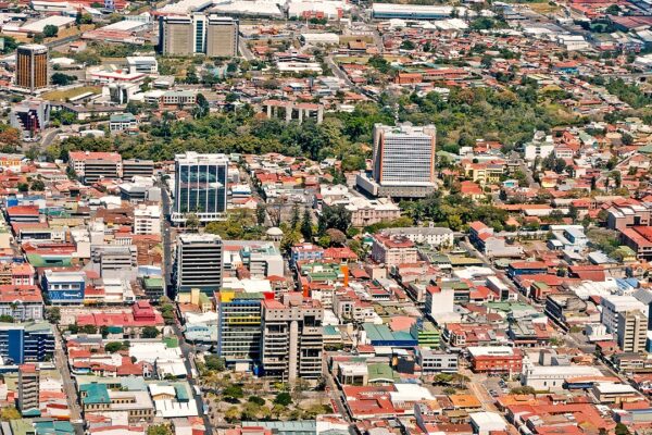 Aerial view of downtown San José, Costa Rica, with office towers and red-roofed low-rise buildings among green parks.