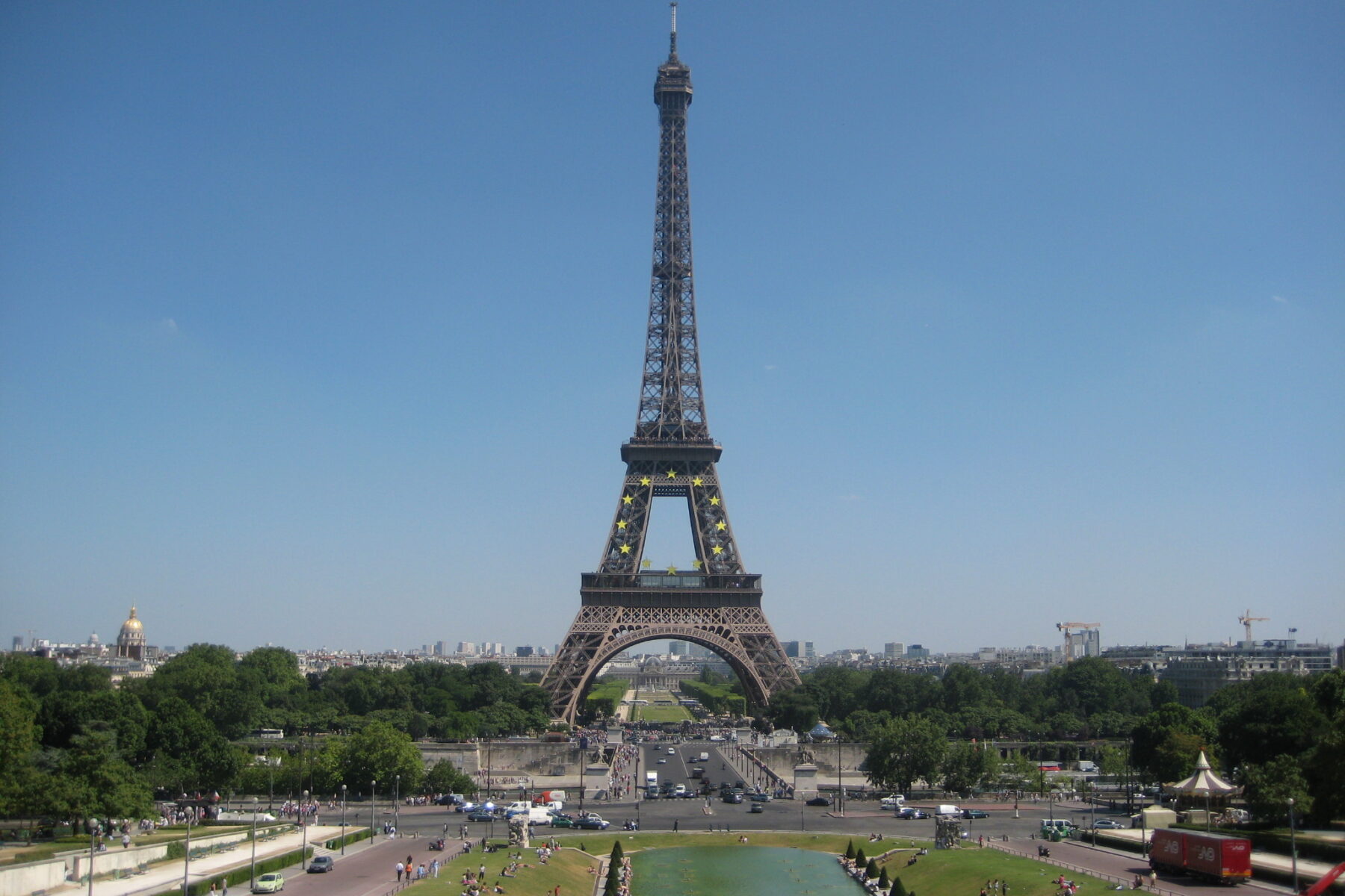The Eiffel Tower under a clear blue sky, seen from the Trocadéro gardens with fountains and lawns in the foreground
