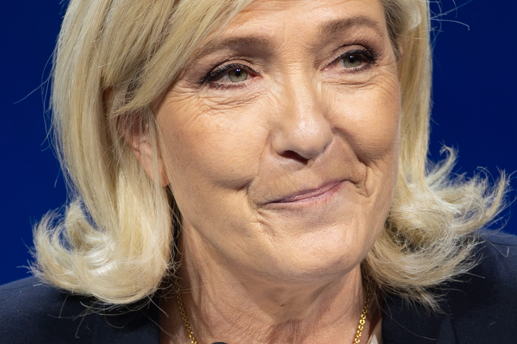 Marine Le Pen smiles behind two microphones in front of a dark blue backdrop