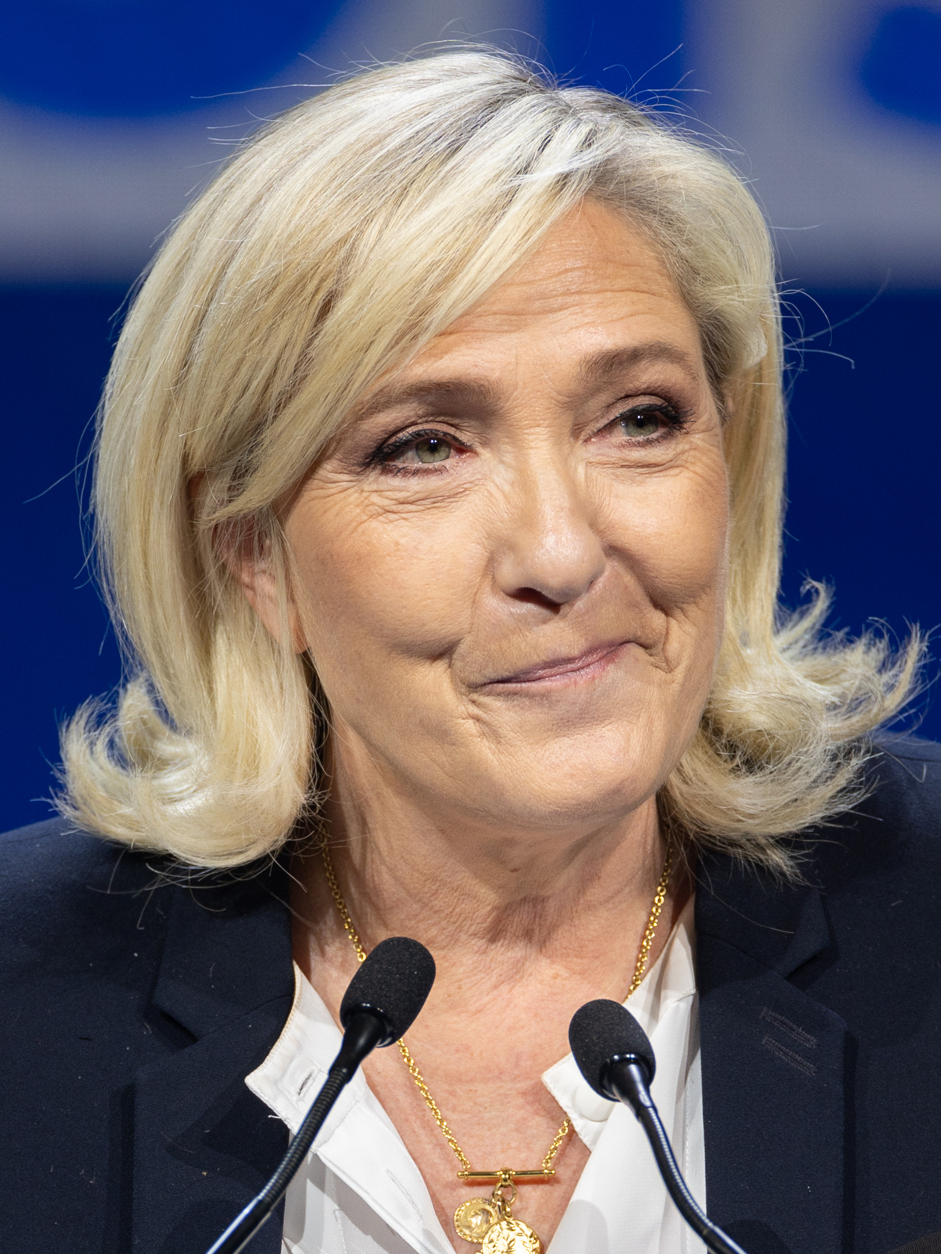 Marine Le Pen smiles behind two microphones in front of a dark blue backdrop