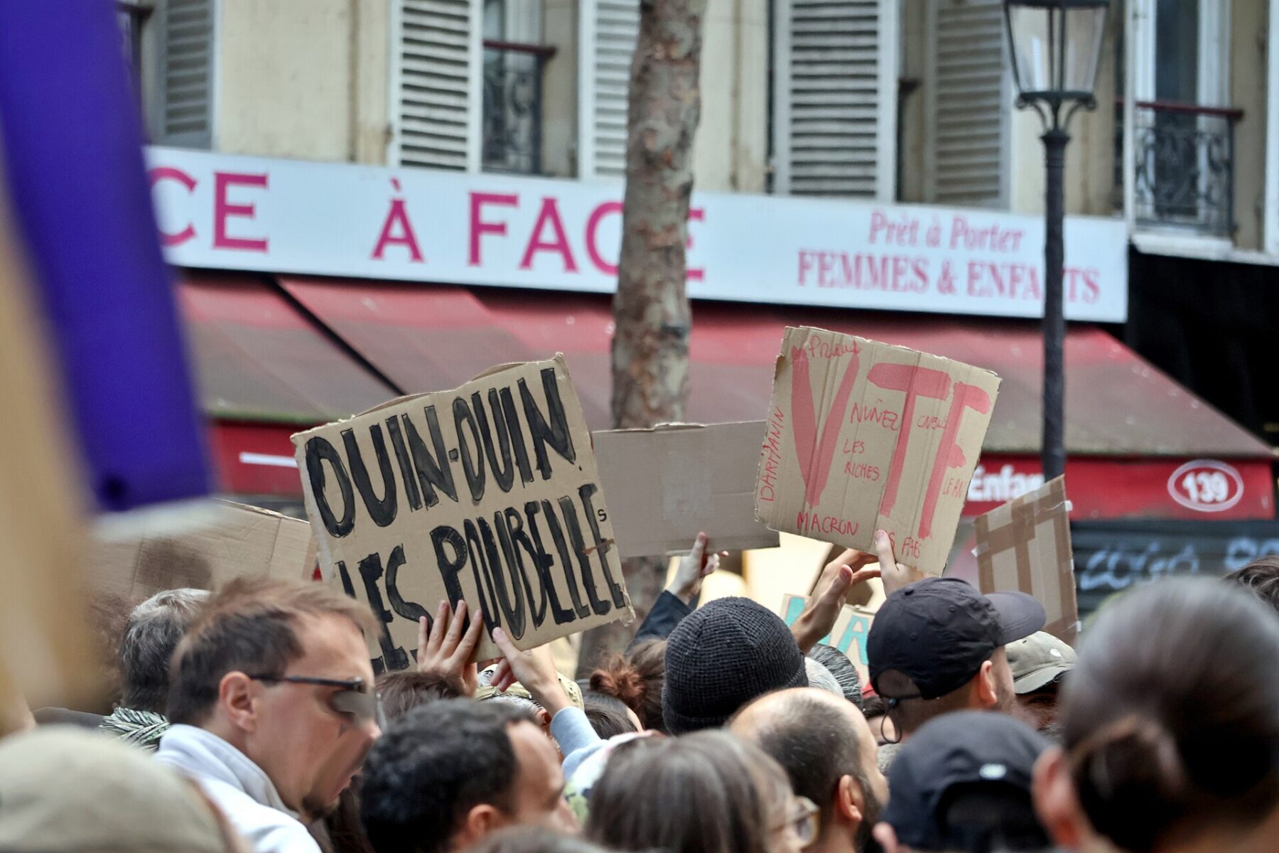 Protesters in a Paris street hold up handwritten cardboard placards, one of them naming Macron