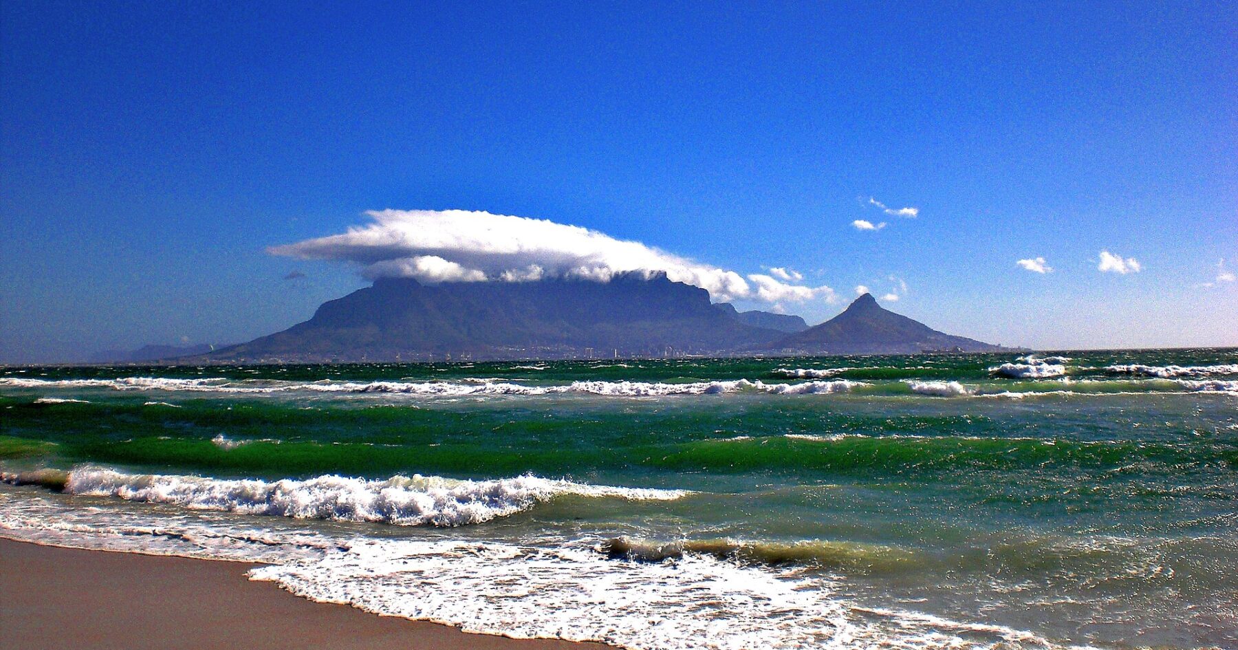 Table Mountain under a cap of cloud, seen across Table Bay from a beach north of Cape Town