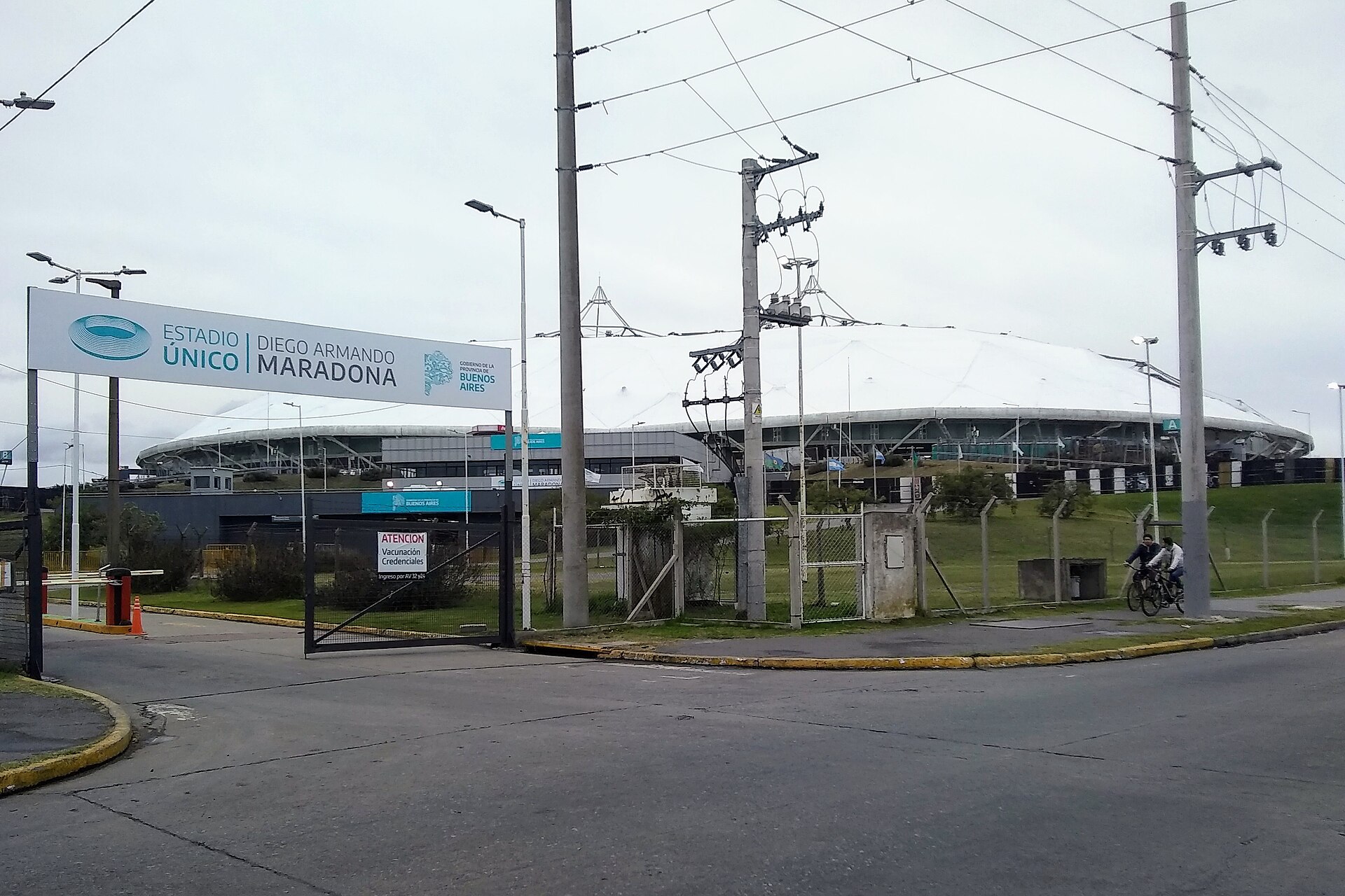 Entrance gate and sign reading Estadio Único Diego Armando Maradona, with the stadium's white roof behind
