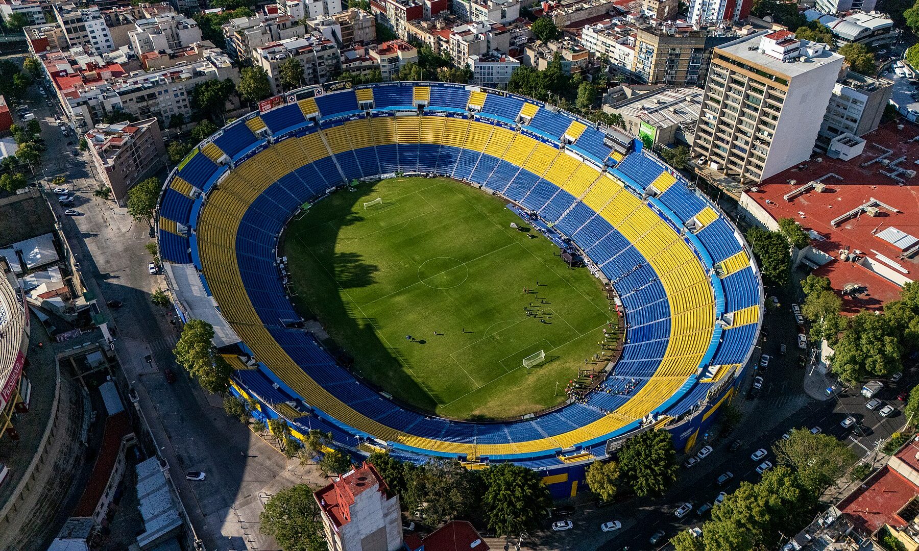 Aerial view of the Estadio Ciudad de los Deportes in Mexico City, with blue and yellow stands around the pitch and apartment blocks on all sides