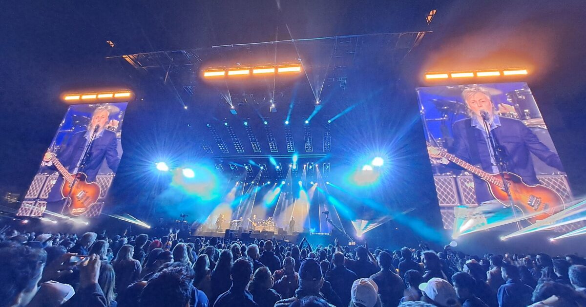 Stadium concert at Estadio GNP Seguros in Mexico City at night, with a crowd in the foreground, a lit stage and two large video screens showing the performer