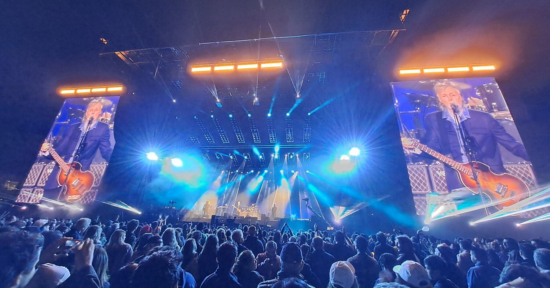 Stadium concert at Estadio GNP Seguros in Mexico City at night, with a crowd in the foreground, a lit stage and two large video screens showing the performer