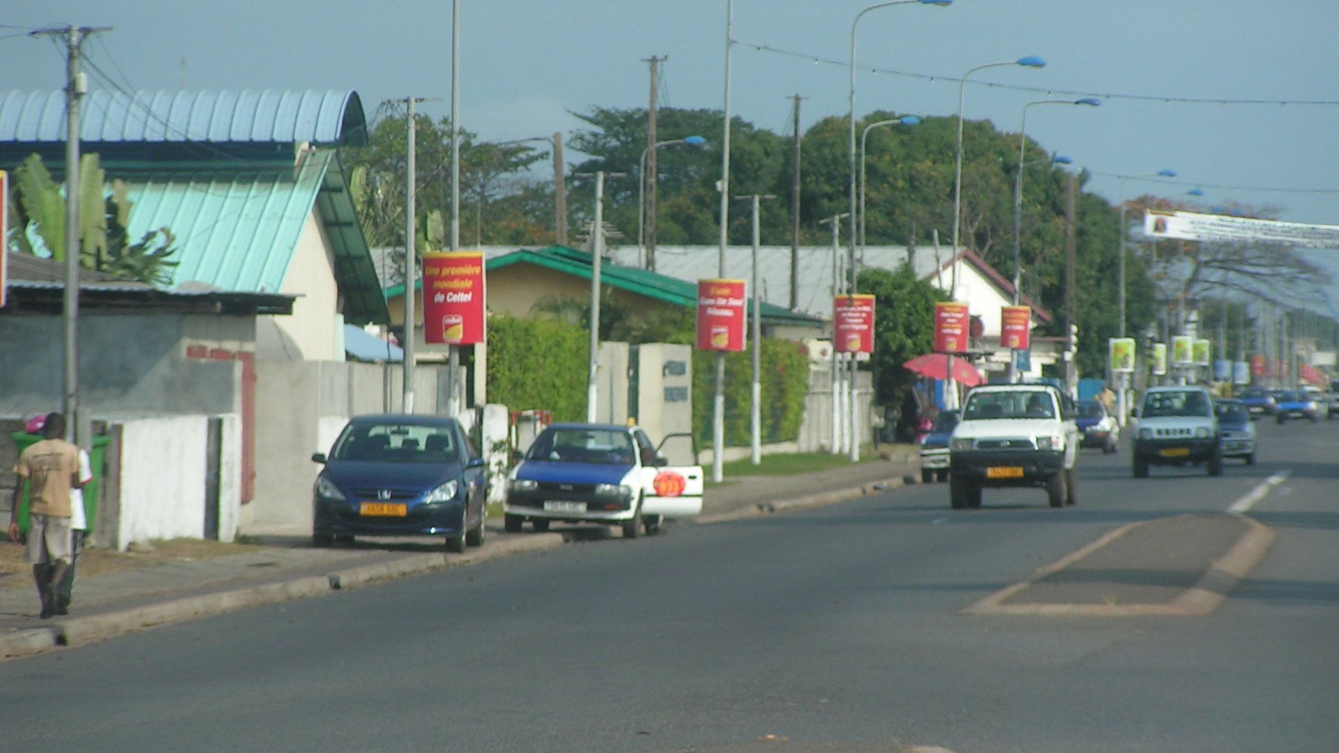 A paved street lined with lamp posts, parked cars and houses in Port-Gentil, Gabon, in 2007