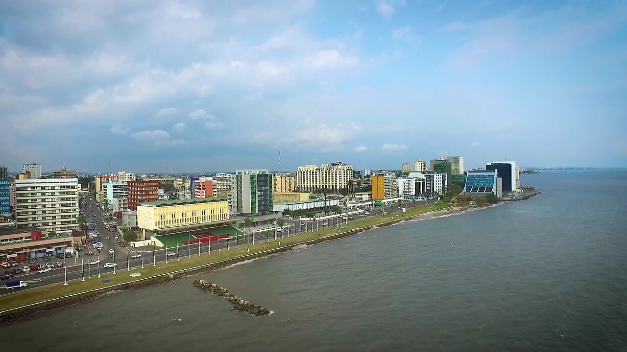 Seafront road in central Libreville lined with lamp posts, office blocks and a stadium beside the water