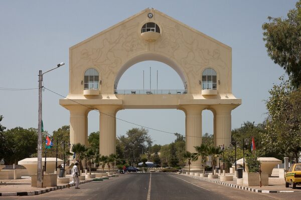 Arch 22, a large cream-coloured memorial arch on a road in Banjul, with a pedestrian and taxis beneath it