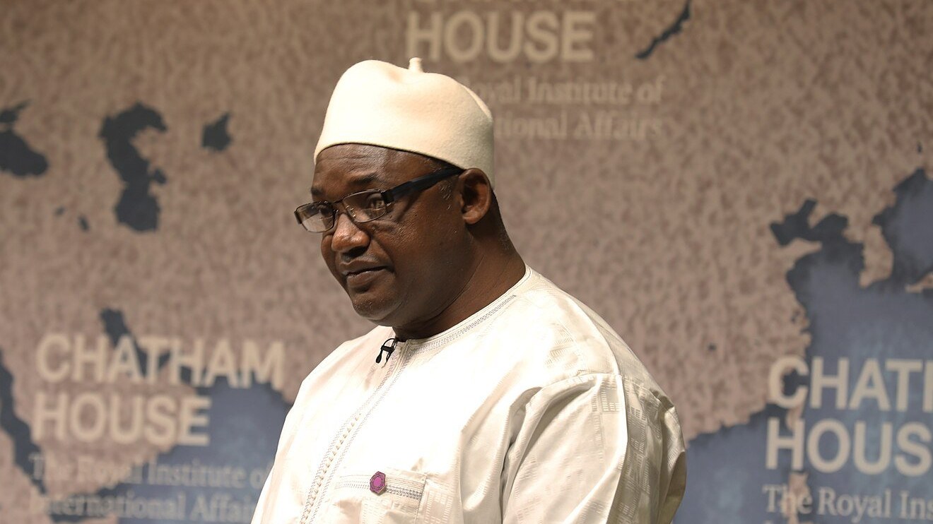 President Adama Barrow of The Gambia in a white traditional robe and cap, speaking at a policy event