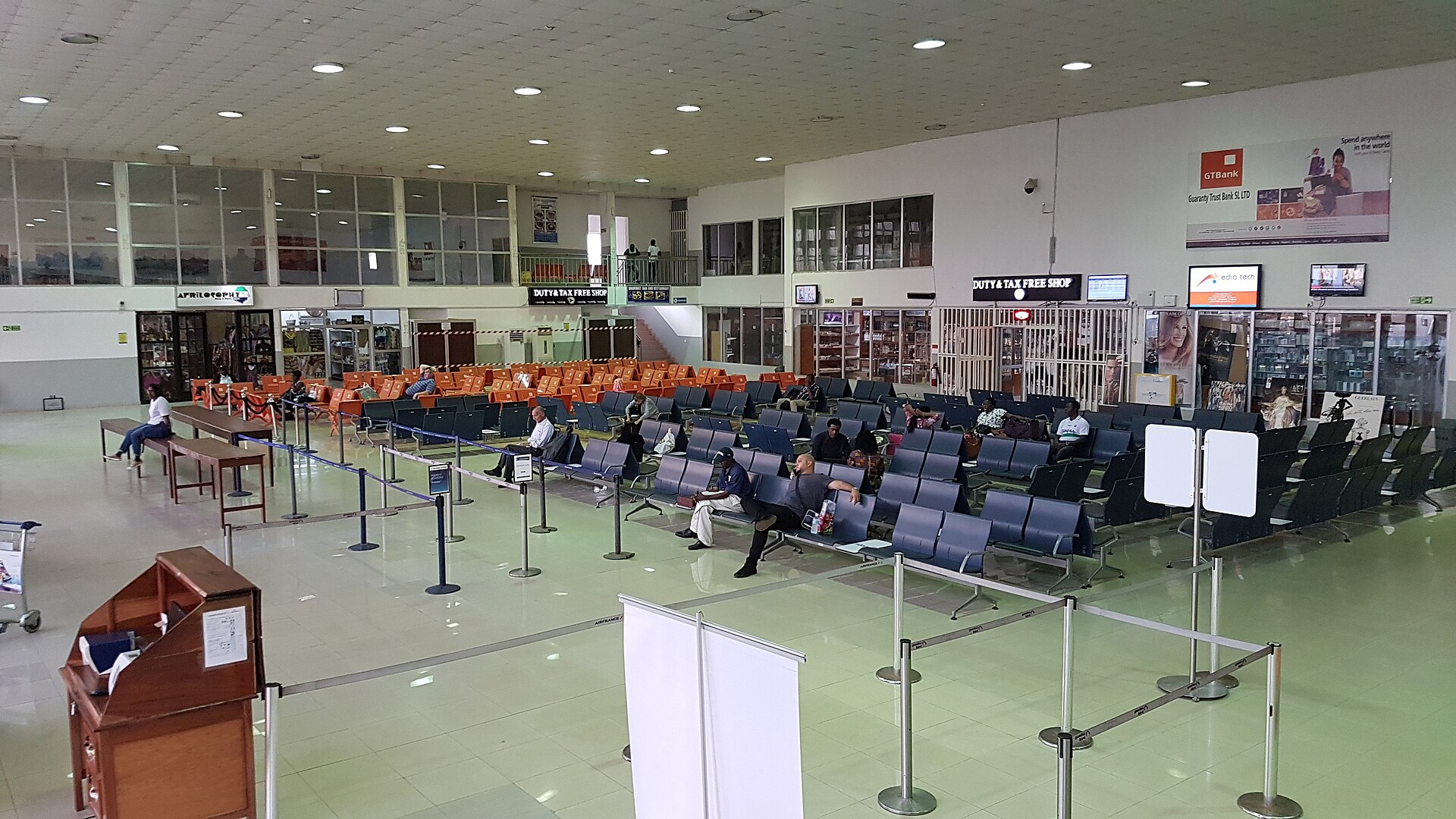 Rows of seats, queue barriers and duty-free shops in the gate area of an airport terminal with few passengers