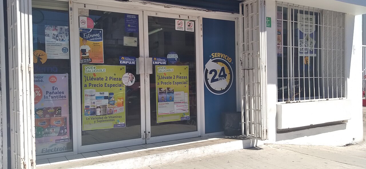 Front doors of a 24-hour pharmacy in Mazatlán, Mexico, with posters for vitamins and supplements