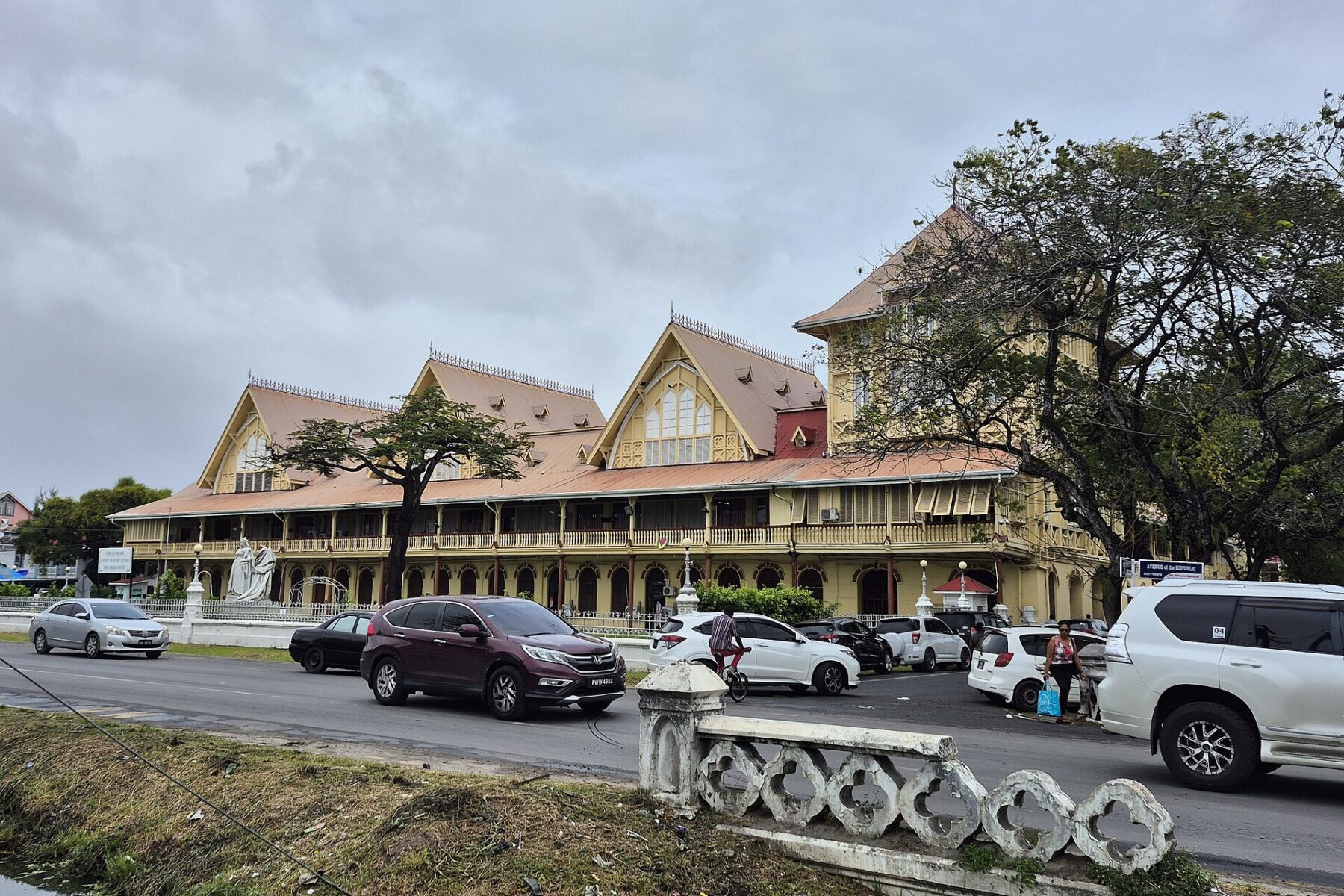 The yellow colonial-era High Court building with steep red roofs in Georgetown, Guyana, with cars passing on the road in front