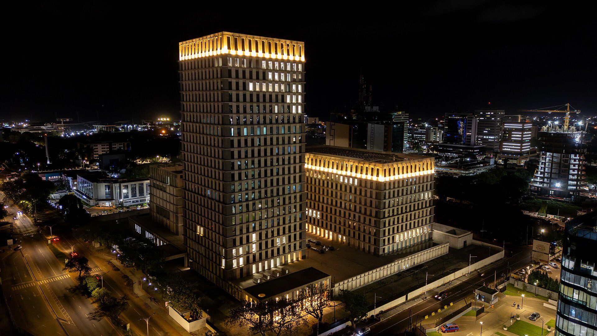 Night view of the Bank Square complex of the Bank of Ghana in Accra, a tall lit tower beside a lower block with city lights behind
